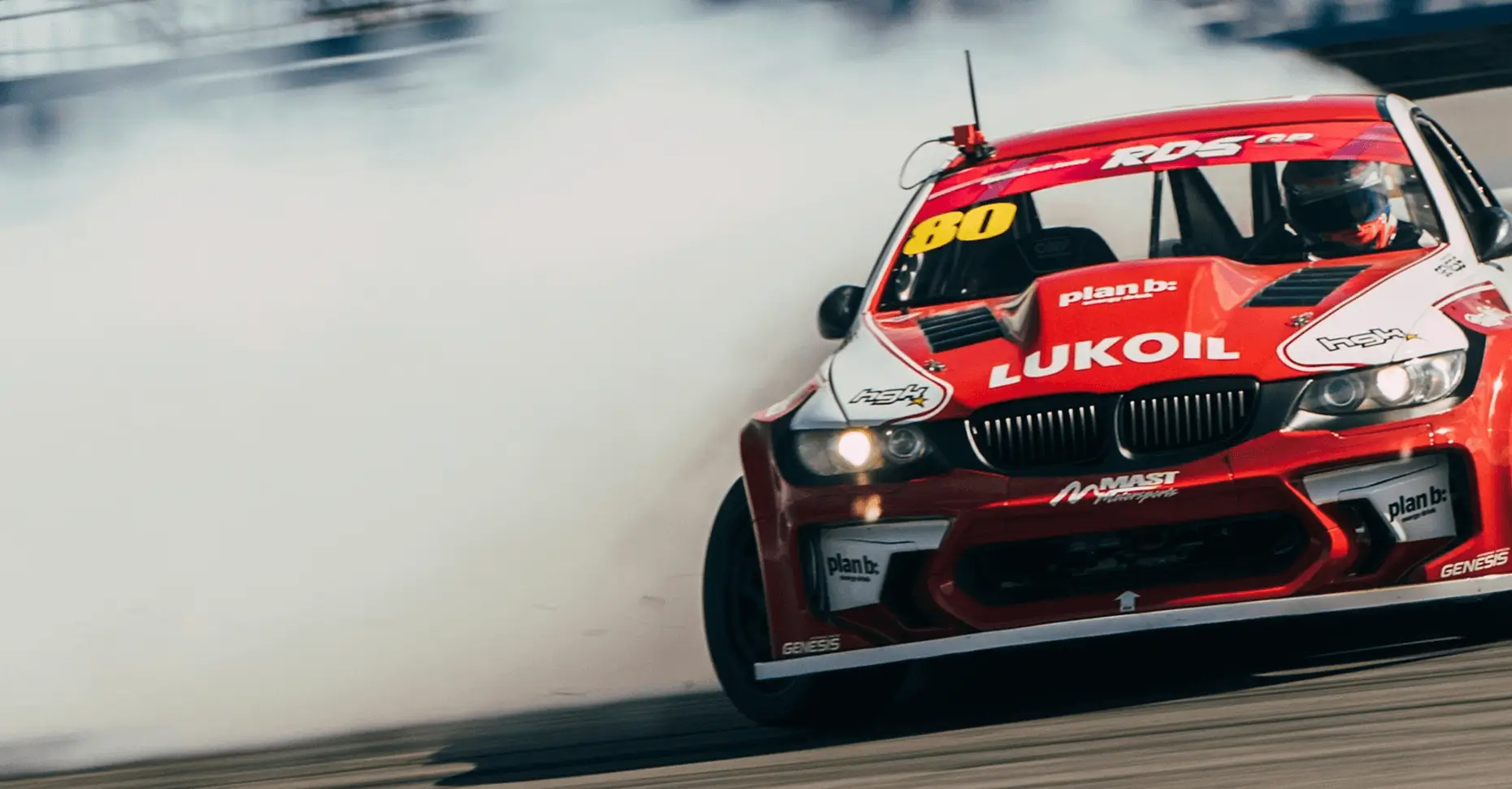 A red Lukoil racing car drifting on track with smoke effects showing dynamic motorsport action